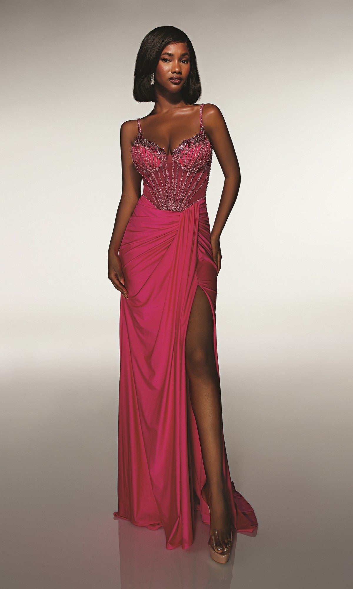 Woman in the Alyce 62113 long prom dress—vibrant pink, sleeveless, with a beaded corset bodice and thigh-high slit—stands against a neutral background.